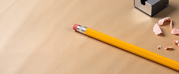Yellow pencil with eraser and shavings on a brown background  