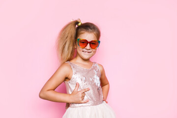 Girl with long hair in festive paper hat and dressy dress on pink background tossing gold confetti