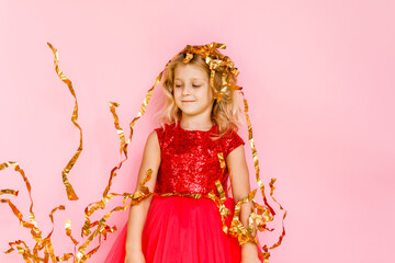 Girl with long hair in festive paper hat and dressy dress on pink background tossing gold confetti
