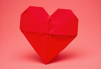 A photographic image of a heart shaped paper origami. The paper is a crisp, matte red, with distinct creases and folds creating a geometric pattern