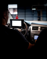 Un técnico automotriz utiliza un dispositivo de diagnóstico portátil conectado al motor de un automóvil. La herramienta muestra datos en pantalla y está enlazada al sistema del coche mediante cables, 