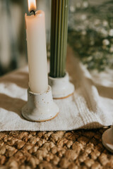 A candle is lit on a table next to a green candle. The tablecloth is white and the candles are placed on a rug