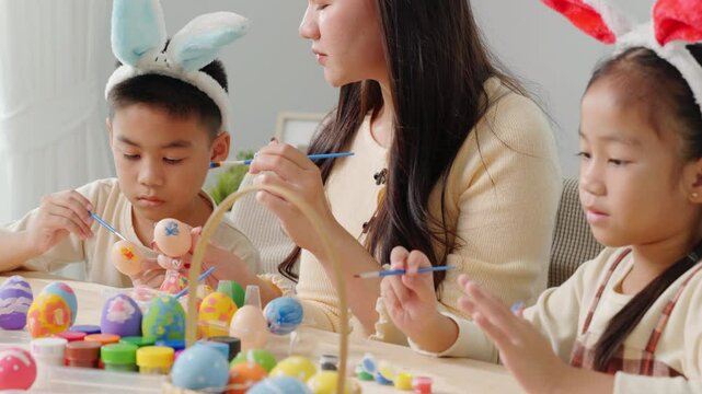 Easter creativity. A mother and kids use a paintbrush to decorate Easter eggs, celebrating spring with fun family activities.