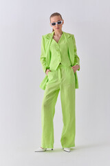 High fashion portrait of young confident female model in green lime color three-piece suit. Monochrome green outfit