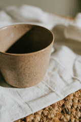 A brown ceramic cup sits on a white cloth. The cup is empty and the cloth is a woven material