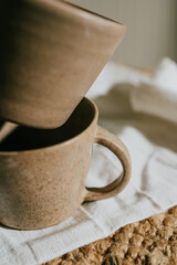 Two cups are sitting on a table, one of which is upside down. The cups are made of a brown material and appear to be ceramic. The scene is simple and uncluttered, with the cups