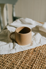 A brown coffee cup sits on a white cloth on a table. The cup is empty and the cloth is made of a woven material. Concept of calm and relaxation, as the cup