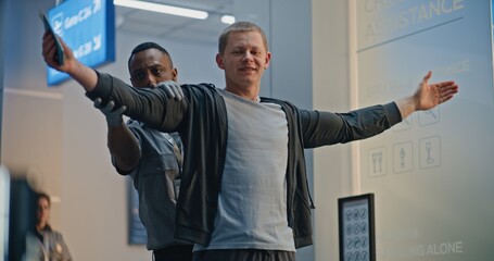 Security Checkpoint: African American TSA Officer Checking Young Man with Prosthetic Leg in Airport...