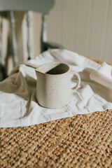 A white ceramic cup sits on a white cloth on a brown rug. The cup is empty and the cloth is folded neatly. Concept of calm and simplicity, with the focus on the simple yet elegant design of the cup