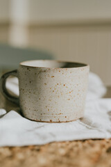 A white ceramic coffee cup with a brown spot on it sits on a white cloth. The cup is placed on a table, and the cloth is folded neatly. Concept of calm and relaxation