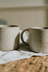 Two white ceramic coffee cups with a white cloth underneath them. The cups are placed on a wooden table