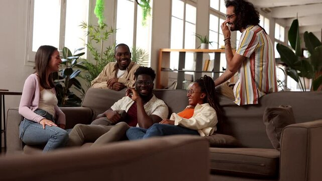 Diverse group of young friends sharing a relaxing moment, sitting together and engaging in conversation on a comfortable sofa in modern apartment setting