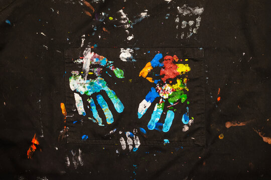 Multicolored handprints in paint on black fabric, on a work art apron, symbol of creativity and expression. Concept of kids art, freedom, color exploration