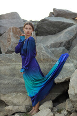 Young slim brunette woman in blue dress standing on the rocks full length
