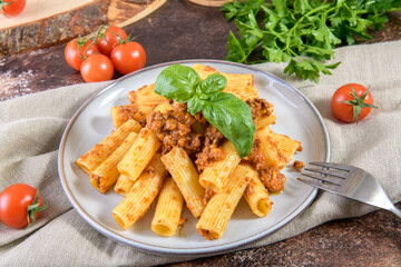 Traditional Rigatoni pasta dish with Bolognese sauce and fresh basil leaves on rustic brown table, close up