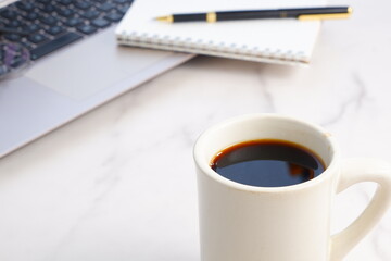 机にノートパソコンやノートを広げ、コーヒーを飲みながらデスクワークをしているイメージ
