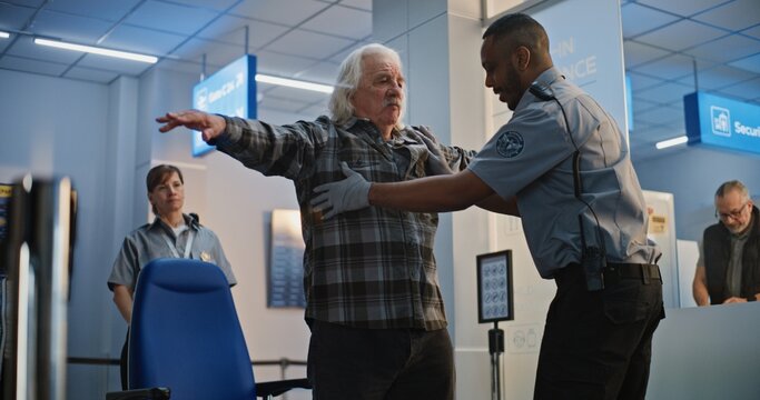 Security Checkpoint in Airport Terminal: African American Security Officer Inspecting Elderly Man Getting Up from Wheelchair. Screening Procedures for Boarding Flight. Senior Tourist with Disability. - Powered by Adobe