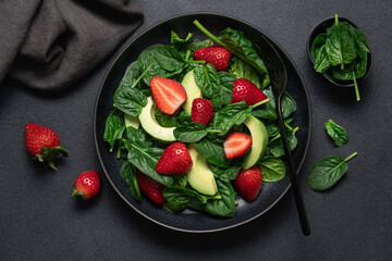 Strawberry salad with avocado and spinach in black plate on dark background. Seasonal dietary healthy salad