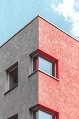 A modern office building's exterior wall is adorned with a geometric pattern of aluminum composite tiles in red, gray, and white, set against a minimalistic background within a vertical frame
