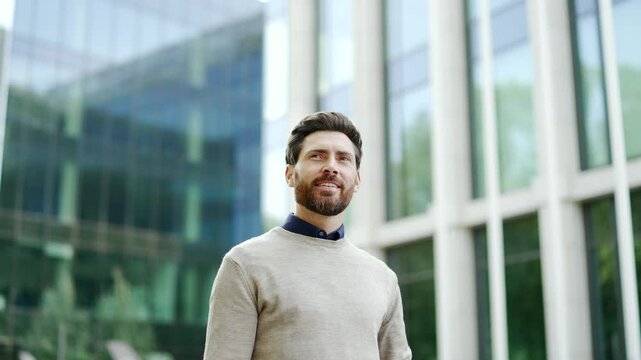Business professional confidently walks outdoors in cityscape near office building. Mature, bearded man enjoys modern urban environment, exuding positivity, success. business life in corporate setting