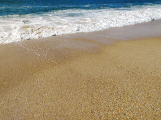 A serene beach at midday with gentle waves lapping the shore and clear blue skies inviting relaxation