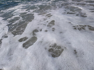 Gentle waves rolling onto sandy beach at sunrise, creating bubbles and a shimmering surface