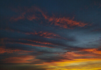 Dramatic sunset sky with layered clouds in hues of orange, pink, and deep blue. Perfect for backgrounds, websites, or atmospheric mood pieces. Evokes feelings of tranquility and wonder.