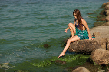 Young brunette woman in bikini sitting on the rock at the sea