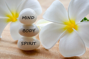 Mind, Body and Spirit text on white zen stones with white flower background