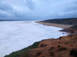 Dramatic seascape featuring powerful waves crashing onto a sandy beach under an overcast sky. Evokes feelings of natures power, solitude, and the raw beauty of the coastline.
