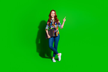 Smiling young woman pointing upward, holding laptop, with vibrant style