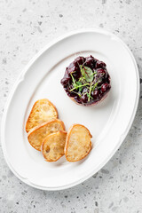A gourmet dish featuring a rich, dark berry compote served over smooth paté, garnished with microgreens, accompanied by slices of toasted bread on a white plate.