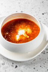 A bowl of rich red soup served with a dollop of cream, showcasing vibrant vegetables in a smooth broth on a textured surface