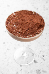 Close-up of a creamy dessert in a glass, topped with cocoa powder, against a white speckled background. Elegant and indulgent, ideal for food and culinary themes.