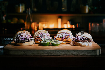 Four sandwiches are on a wooden cutting board, with a lime on each one