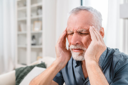 Headache. Senior man suffering from migraine pain massaging temples sitting at home. Healthcare health problems in older age stress and people medicine concept