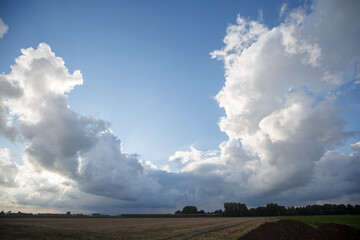 Dramatic cloud formations over a rural landscape during early evening hours with clear blue skies peeking through