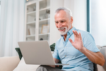 Smiling mature man sit on couch look at camera waving having video call on computer, happy senior grandfather, elderly male talk using new technologies, fast internet connection on gadget