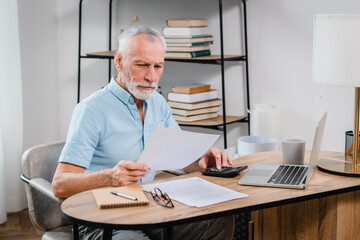 Happy busy older professional businessman entrepreneur using laptop holding bill corporate document...