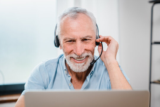 Happy old 60s man in headphones with microphone looking at camera starting online video call conversation, communicating distantly with friends or family, older people and modern technology concept.