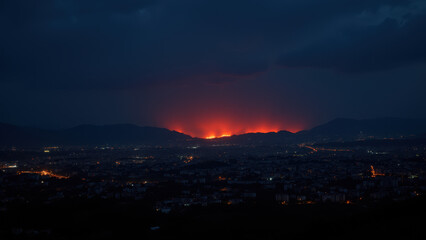 A nighttime view of a city skyline with a wildfire consuming hills and homes in the distance.