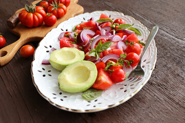 Fresh healthy avocado and tomato salad with onions on dark rustic background .