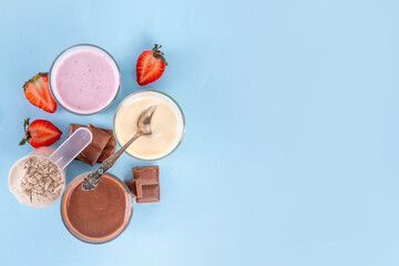 Quick and simple protein pudding. Healthy summer cold dessert. Three glasses with vanilla, chocolate and berry protein pudding, with chocolate slices, fresh strawberry, blueberry, protein powder scoop