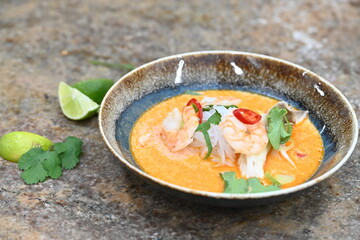 A flavorful and spicy Thai Tom Yum Goong soup with shrimp, rice noodles, and a rich coconut milk broth. Garnished with fresh cilantro and red chili, 