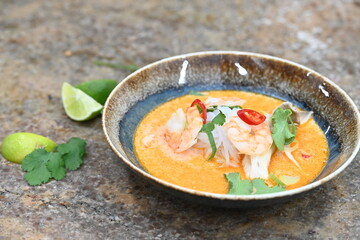 A flavorful and spicy Thai Tom Yum Goong soup with shrimp, rice noodles, and a rich coconut milk broth. Garnished with fresh cilantro and red chili, 