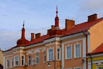 Fototapeta premium An architectural shot of a historical building with red roofs and elegant spires. The facade of the building is done in warm, pastel tones with white window frames, creating an elegant contrast.