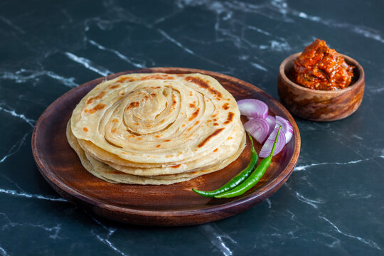 Crispy, flaky laccha paratha served hot with tangy pickle, fresh onion slices, and spicy green chili for a perfect flavor burst.