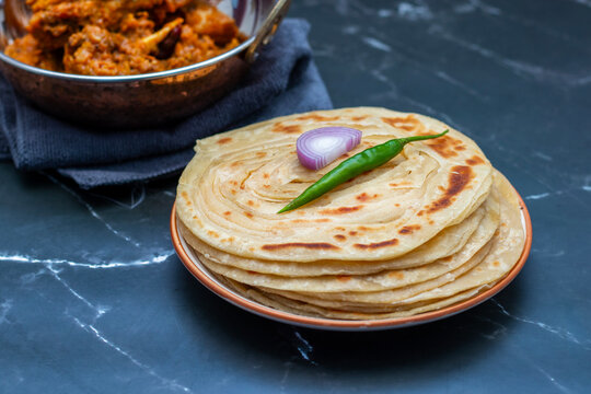 Crispy, flaky laccha paratha served hot with tangy pickle, fresh onion slices, and spicy green chili for a perfect flavor burst.
