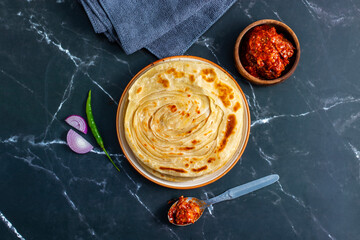 Crispy, flaky laccha paratha served hot with tangy pickle, fresh onion slices, and spicy green...