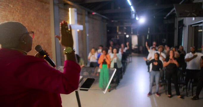 Energetic pastor addressing a diverse congregation, delivering a passionate sermon in a modern church setting with a glowing cross on a brick wall backdrop